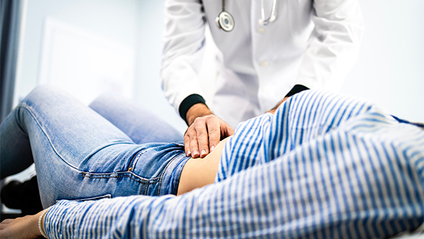 Doctor examining a patient's abdomen while they lie on an examination table.